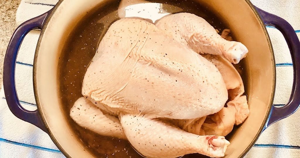Whole Chicken in a Dutch Oven salted and peppered with water for roasting in the oven.