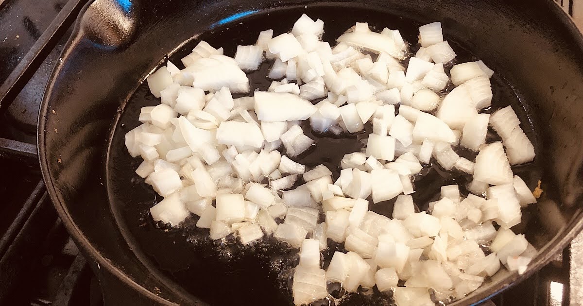 Diced onions in a cast iron skillet being sauteed for chicken gravy.