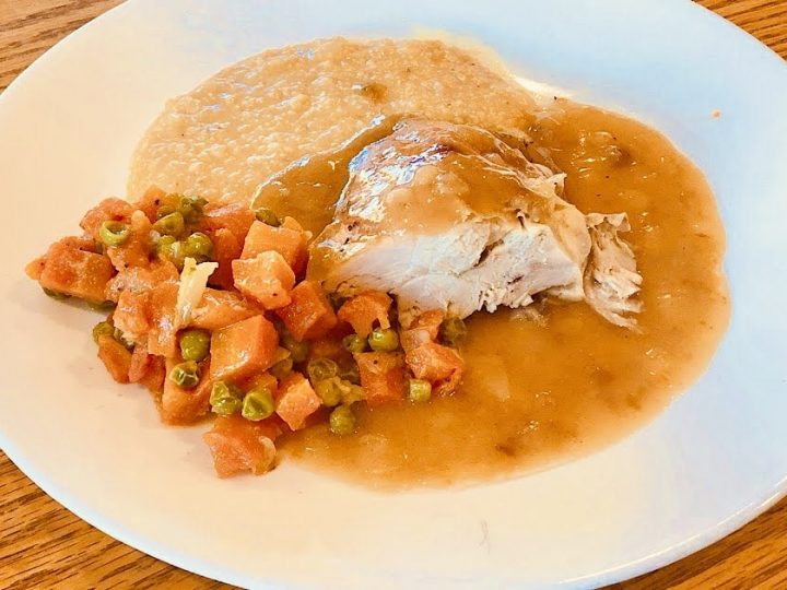 Roasted chicken plated with grits and onion gravy along with peas and carrots