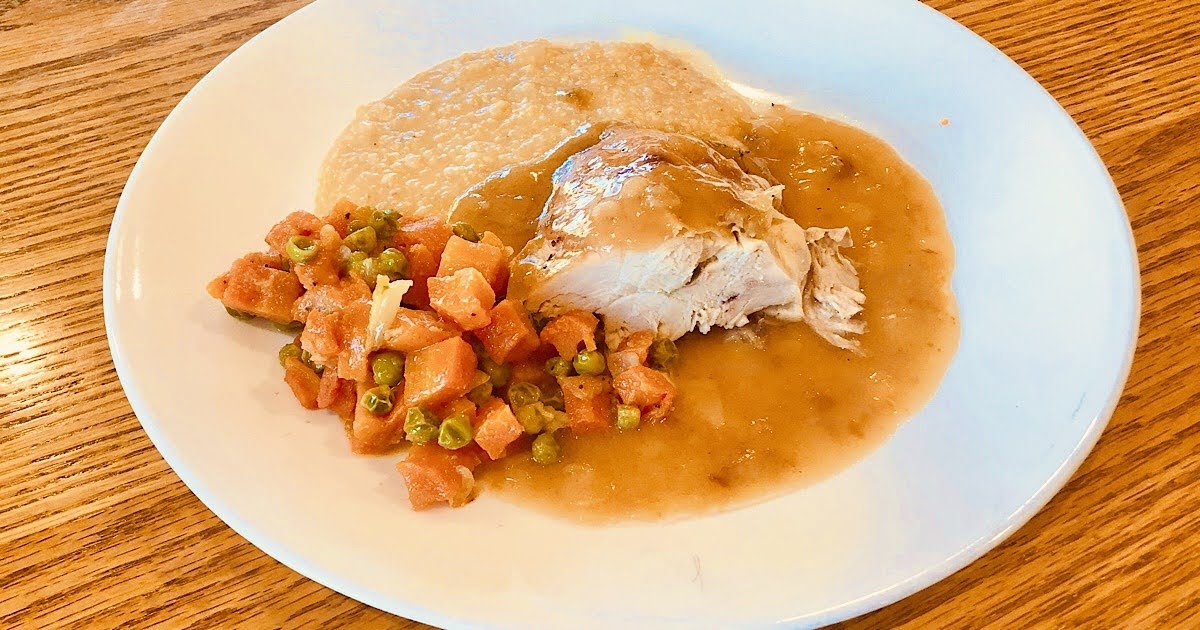 Roasted chicken plated with grits and onion gravy along with peas and carrots