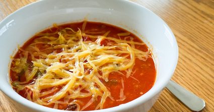 A bowl of stuffed pepper soup topped with cheddar cheese.