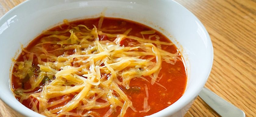 A bowl of stuffed pepper soup topped with cheddar cheese.